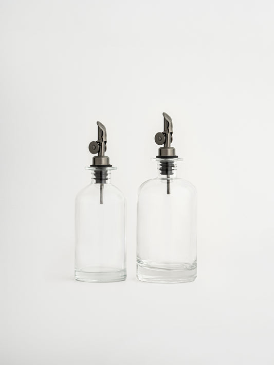 Dispensers voor olie en azijn in twee maten met smoke zwarte schenktuit. Glazen fles met stijlvolle en praktische schenktuit voor nauwkeurig schenken zonder druppelen. Ideaal voor olijfolie, azijn of sojasaus. Minimalistisch design voor een moderne keuken. Keukenaccessoire voor op het aanrecht of eettafel. Past perfect bij een georganiseerde keuken of pantry. Luchtdichte afsluiting en gecontroleerde dosering.