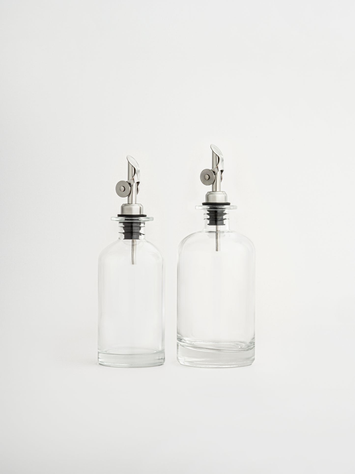 oliedispenser zilveren dop, azijndispenser zilveren schenktuit, glazen fles voor olie en azijn, dispenser in twee maten, olijfoliefles, azijnfles keuken, glazen oliedispenser, keukenaccessoire olie, zilveren schenktuit, keuken organizer fles, moderne keukenfles, luchtdichte oliefles, nauwkeurig schenken, stijlvolle dispenser, glazen voorraadfles, olie en azijn set, zilveren keukenaccessoire