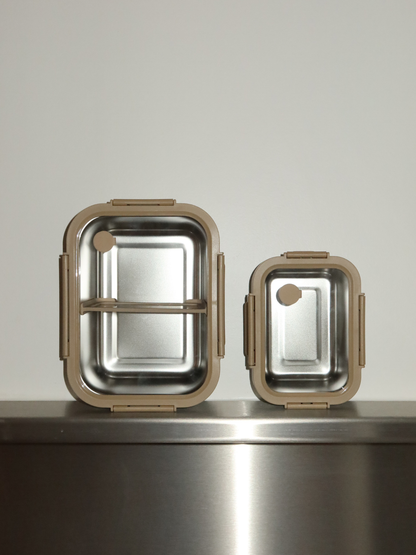 Leicht, auslaufsicher und lebensmittelsicher: Bento ist ein praktischer, dennoch eleganter Behälter aus Edelstahl mit transparentem Kunststoffdeckel, herausnehmbarem Trenner und feinen beigen Details. Sicherungsclips sorgen für einen festen Verschluss bei Meal Prep, Resten oder trockenen Zutaten. Ungiftig, BPA-frei und langlebig – Bento verbindet Einfachheit mit Funktionalität. Seine sanften Farbtöne und der durchsichtige Deckel bringen Ruhe und Stil in jede Küche, Speisekammer oder Lunchbox.