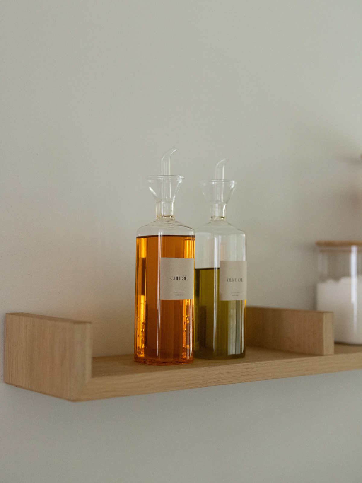 Transparenter Öl- und Essigspender Vivi, ein stilvolles Set aus zwei Glasflaschen für Öl, Essig und andere flüssige Würzmittel. Das klare Design macht den Inhalt leicht erkennbar und sorgt für eine aufgeräumte, minimalistische Optik in der Küche oder auf dem Esstisch. Ideal für Olivenöl, Balsamico, Dressings und Saucen – zum Kochen oder Servieren. Passende „Oil“- und „Vinegar“-Etiketten sind separat erhältlich und sorgen für noch mehr Ordnung.